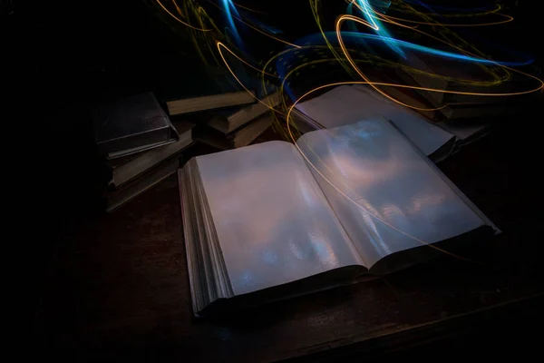 A stack of old books. Vintage book on wooden table. Magic lightning around a glowing book in the room of darkness. Selective focus