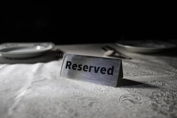 Reserved sign on the table. A tag of reservation placed on the wood table. Metal tag with reservation on dark. Reserved table in a restaurant. Creative concept with colorful lights. Selective focus