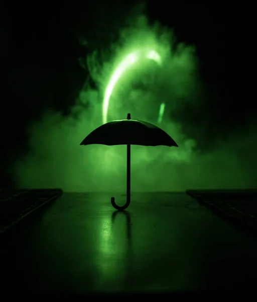 Silhouette of umbrella miniature on table with dark toned foggy background. Creative concept. Selective focus