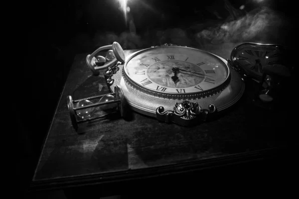 Time concept. Big vintage round clock on wooden table with abstract light. Dark atmosphere. Creative decoration. Selective focus