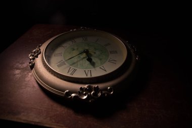 Zaman kavramı. Soyut ışıkla ahşap masada büyük klasik yuvarlak saat. Karanlık atmosfer. Yaratıcı dekorasyon. Seçici odak