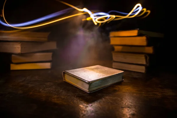 A stack of old books. Vintage book on wooden table. Magic lightning around a glowing book in the room of darkness. Selective focus