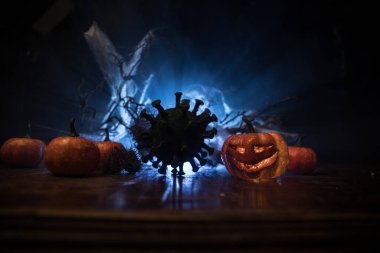 Corona virüsü küresel pandemik konsepti sırasında Cadılar Bayramı. Karanlıkta parlayan balkabakları ve Covid romanı tematik ürkütücü süslemelerle. Cadılar Bayramı balkabağı sisli arka planda. Seçici odak