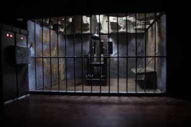 Uygulama kavramı. Eski hapishanenin seçici odak noktasında idam cezası elektrikli sandalye minyatürü. Eski hapishane parmaklıkları hücre kilidi. Yaratıcı sanat dekorasyonu. Karanlıkta elektrikli sandalye ölçeği modeli