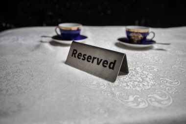 Masaya ayırtılmış tabela. Ahşap masaya bir etiket yerleştirilmiş. Karanlıkta rezervasyonu olan metal etiket. Bir restoranda rezervasyon masası. Renkli ışıklarla yaratıcı bir kavram. Seçici odak