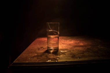 İçki, kırık cam konsepti. Ahşap masada kırık bardaklar, sisli, koyu tonlu arka plan. Seçici odak