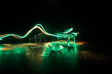 İçki, kırık cam konsepti. Ahşap masada kırık bardaklar, sisli, koyu tonlu arka plan. Seçici odak