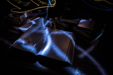 Bir yığın eski kitap. Ahşap masanın üzerinde antika bir kitap. Karanlıkta parlayan bir kitabın etrafında sihirli bir yıldırım. Seçici odak