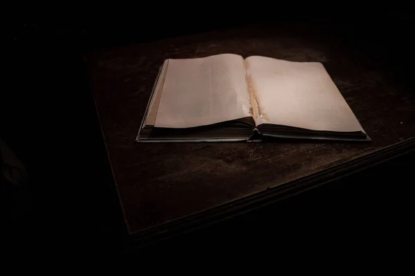 A stack of old books. Vintage book on wooden table. Magic lightning around a glowing book in the room of darkness. Selective focus