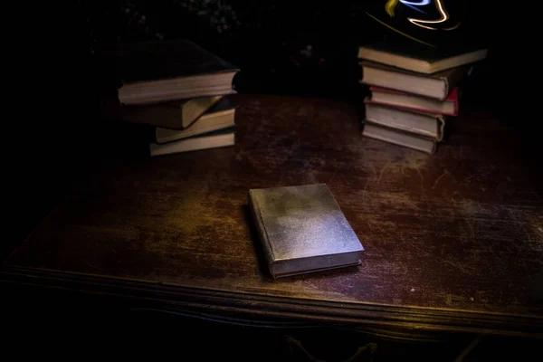 A stack of old books. Vintage book on wooden table. Magic lightning around a glowing book in the room of darkness. Selective focus