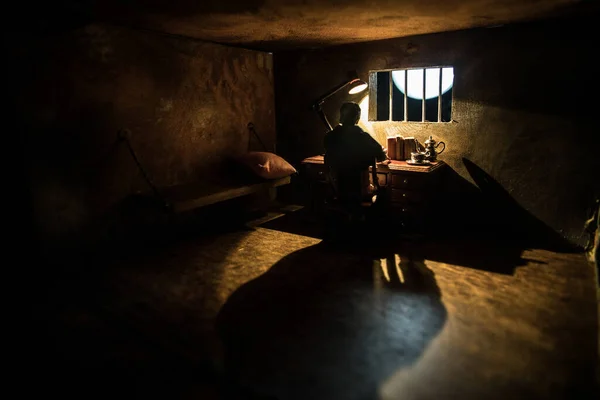 Man in prison man behind bars concept. Old dirty grunge prison miniature. Dark prison interior creative decoration. Miniature table inside. Selective focus