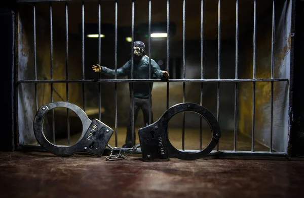 Man in prison man behind bars concept. Old dirty grunge prison miniature. Dark prison interior creative decoration with handcuffs. Selective focus