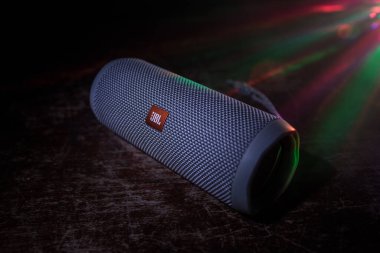 BAKU. AZERBAIJAN - 28.07.2020: JBL Flip 4 Bluetooth Hoparlörü, ahşap masaya yakın çekim, renkli ışıklar ve arka planda sis. Seçici odak