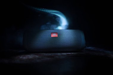 BAKU. AZERBAIJAN - 28.07.2020: JBL Flip 4 Bluetooth Hoparlörü, ahşap masaya yakın çekim, renkli ışıklar ve arka planda sis. Seçici odak