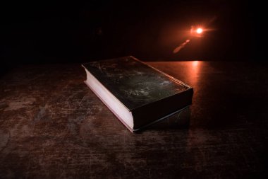 Bir yığın eski kitap. Ahşap masanın üzerinde antika bir kitap. Karanlıkta parlayan bir kitabın etrafında sihirli bir yıldırım. Seçici odak
