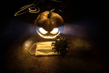 Corona virüsü küresel pandemik konsepti sırasında Cadılar Bayramı. Karanlıkta parlayan balkabakları ve Covid romanı tematik ürkütücü süslemelerle. Cadılar Bayramı balkabağı sisli arka planda. Seçici odak