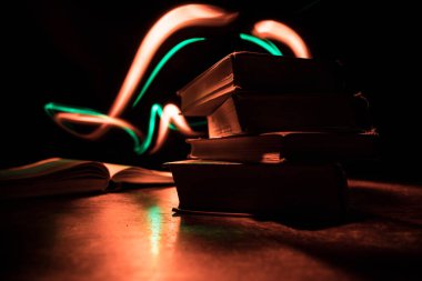Bir yığın eski kitap. Ahşap masanın üzerinde antika bir kitap. Karanlıkta parlayan bir kitabın etrafında sihirli bir yıldırım. Seçici odak