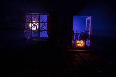 Cadılar Bayramı korku kavramı ve parlayan balkabağı. Geceleri mobilyaları, kapısı ve penceresi olan gerçekçi bir bebek evi oturma odası. Dışarıda korkunç zombiler var. Seçici odak.