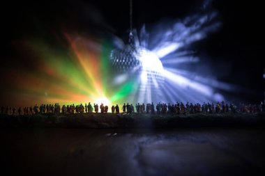 Kulüp hayatı yaratıcı konsepti. Kalabalık minyatür, büyük disko ayna topunun önünde ışıklarla dikiliyor. Gece kulübü geçmişi. Parti ışıkları disko topu ve kulüp üyeleri. Seçici odak