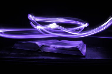 Bir yığın eski kitap. Ahşap masanın üzerinde antika bir kitap. Karanlıkta parlayan bir kitabın etrafında sihirli bir yıldırım. Seçici odak