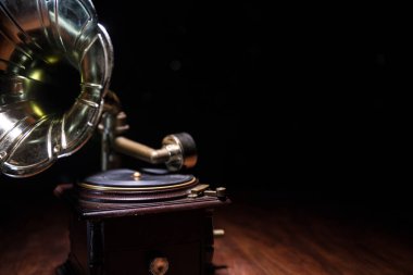 Müzik konsepti. Karanlık bir arka planda eski bir gramofon. Ahşap masanın üzerinde ton lambalı bir disk olan gramofon. Seçici odak