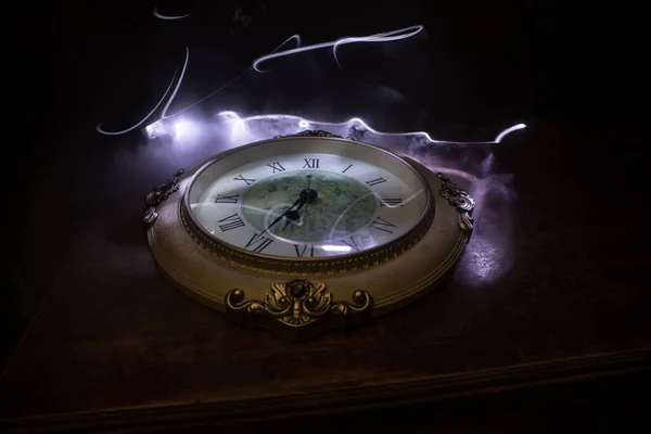 Time concept. Big vintage round clock on wooden table with abstract light. Dark atmosphere. Creative decoration. Selective focus