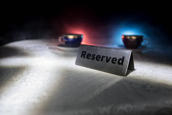 Reserved sign on the table. A tag of reservation placed on the wood table. Metal tag with reservation on dark. Reserved table in a restaurant. Creative concept with colorful lights. Selective focus