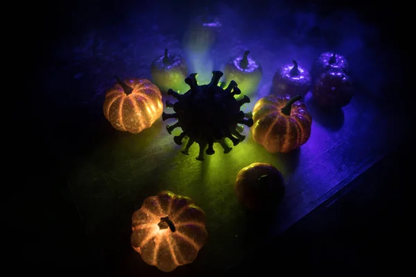 Halloween during Corona virus global pandemic concept. Glowing pumpkins and Covid novel on dark with thematic spooky decorations. Halloween pumpkin on foggy backlight. Selective focus