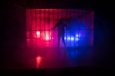 Hapisteki adam demir parmaklıklar arkasında. Eski edepsiz hapishane minyatürü. Karanlık hapishane iç dekorasyonu. Kırmızı mavi polis ışıklarıyla. Seçici odak