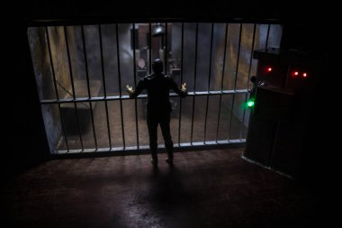 Uygulama kavramı. Eski hapishanenin seçici odak noktasında idam cezası elektrikli sandalye minyatürü. Eski hapishane parmaklıkları hücre kilidi. Yaratıcı sanat dekorasyonu. Karanlıkta elektrikli sandalye ölçeği modeli