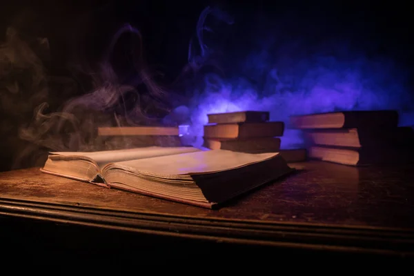 A stack of old books. Vintage book on wooden table. Magic lightning around a glowing book in the room of darkness. Selective focus