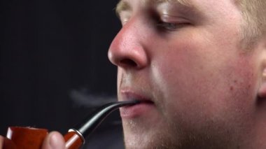 bir adam pipoyla sigara içiyor.
