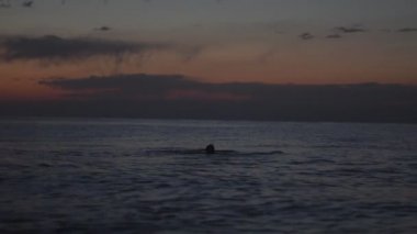 bir adam günbatımında yüzüyor