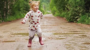 Çocuk kauçuk botlarda su birikintileri üzerinden çalışır