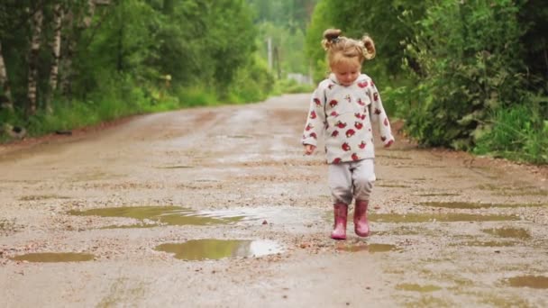 Het kind loopt door plassen in rubberen laarzen — Stockvideo