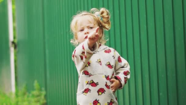 Una niña pequeña parada en el pueblo junto a la valla — Vídeos de Stock