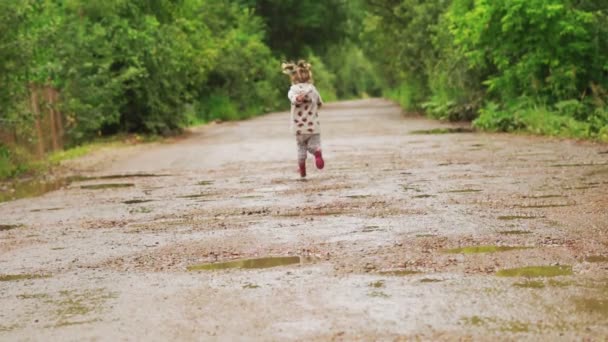 El niño corre a través de charcos en botas de goma — Vídeo de stock
