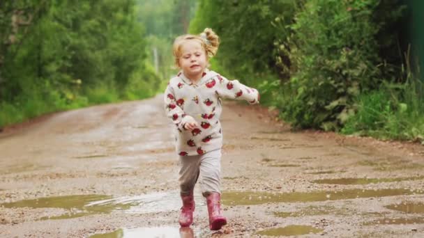 A criança corre através de poças em botas de borracha — Vídeo de Stock