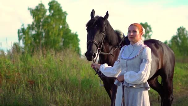 En flicka i en gammal klänning bredvid en häst — Stockvideo