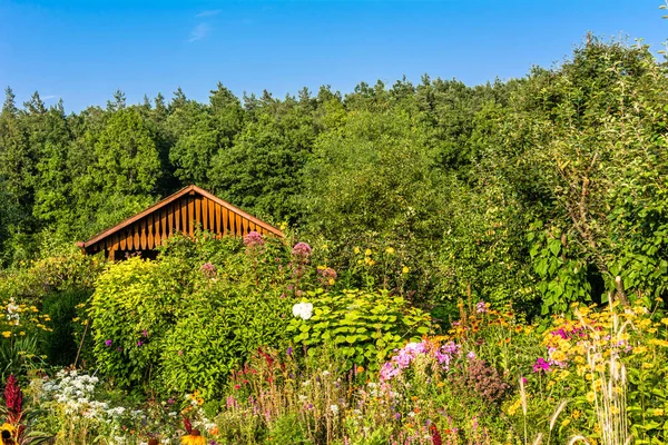 Wooden cottage in garden scenery with a small garden house, flowers and trees