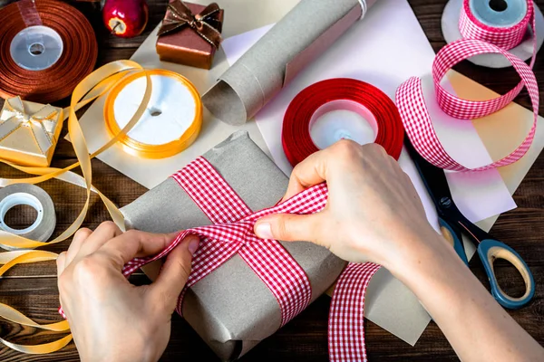 Wrapping christmas gift with paper, detail of hands and ribbons for packing presents