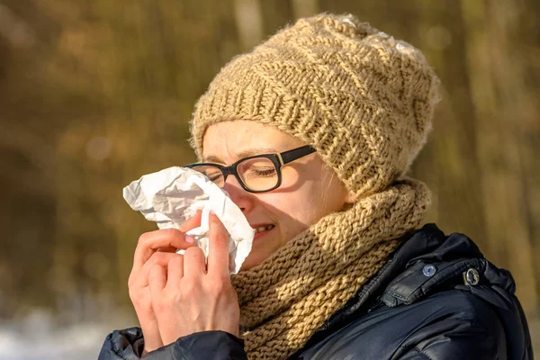 Woman with cold sneezing in a tissue and blowing her nose. Sick people with flu, concept autumn outdoor