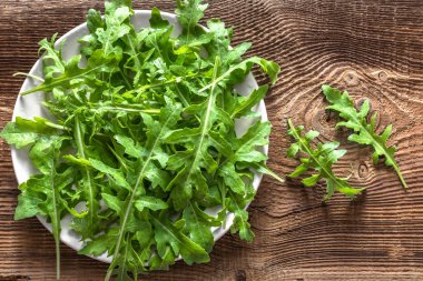 Taze roka yaprakları, yeşil sebzeler, yapraklar, rucola ahşap arka plan üzerinde plaka üzerinde