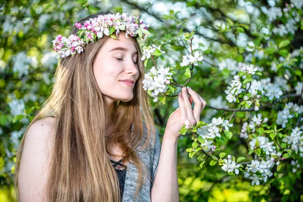 Outdoor fashion with beautiful face of woman smelling flower. Girl in spring blossoms enjoying in the garden.