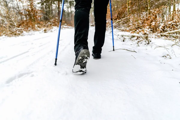 Woman hiking in snow. Boots and legs detail. Outdoor activity, winter walk in snow with nordic walking sticks.