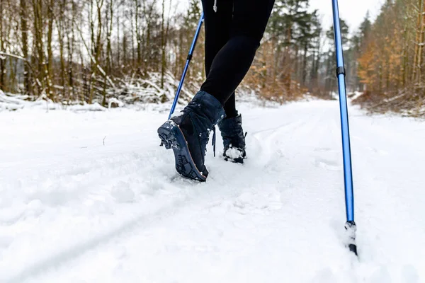 Active person walking in snow. Shoes and legs detail. Outdoor activity, winter sport on snow with trekking sticks.