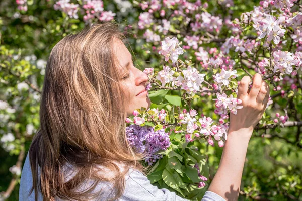 Piękna kobieta wśród kwitnących drzew pachnąca kwitnącą gałąź jabłka w wiosennym ogrodzie — Zdjęcie stockowe