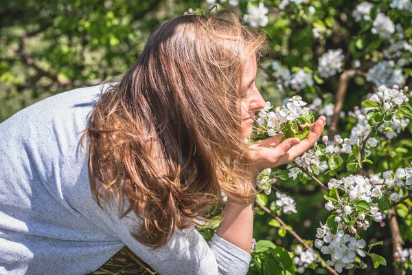 Piękna kobieta pachnąca kwiatami wśród wiosennych kwitnących drzew — Zdjęcie stockowe