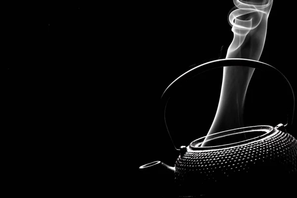 Antique teapot with steaming hot tea on black background.