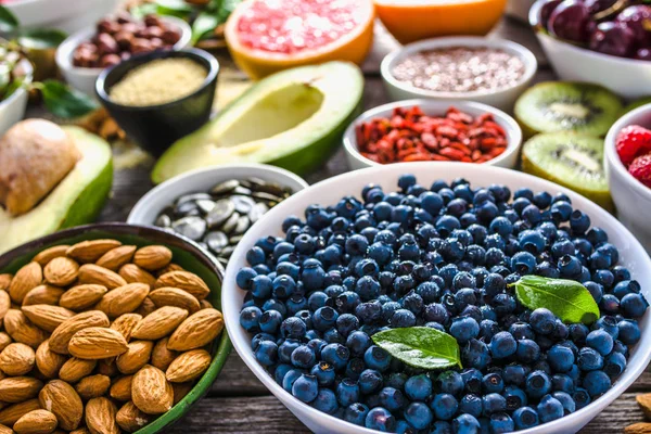 Arándanos frescos y otros alimentos saludables en la mesa. Desayuno en cuencos con superalimentos, dieta orgánica con frutas, frutos secos y bayas . — Foto de Stock